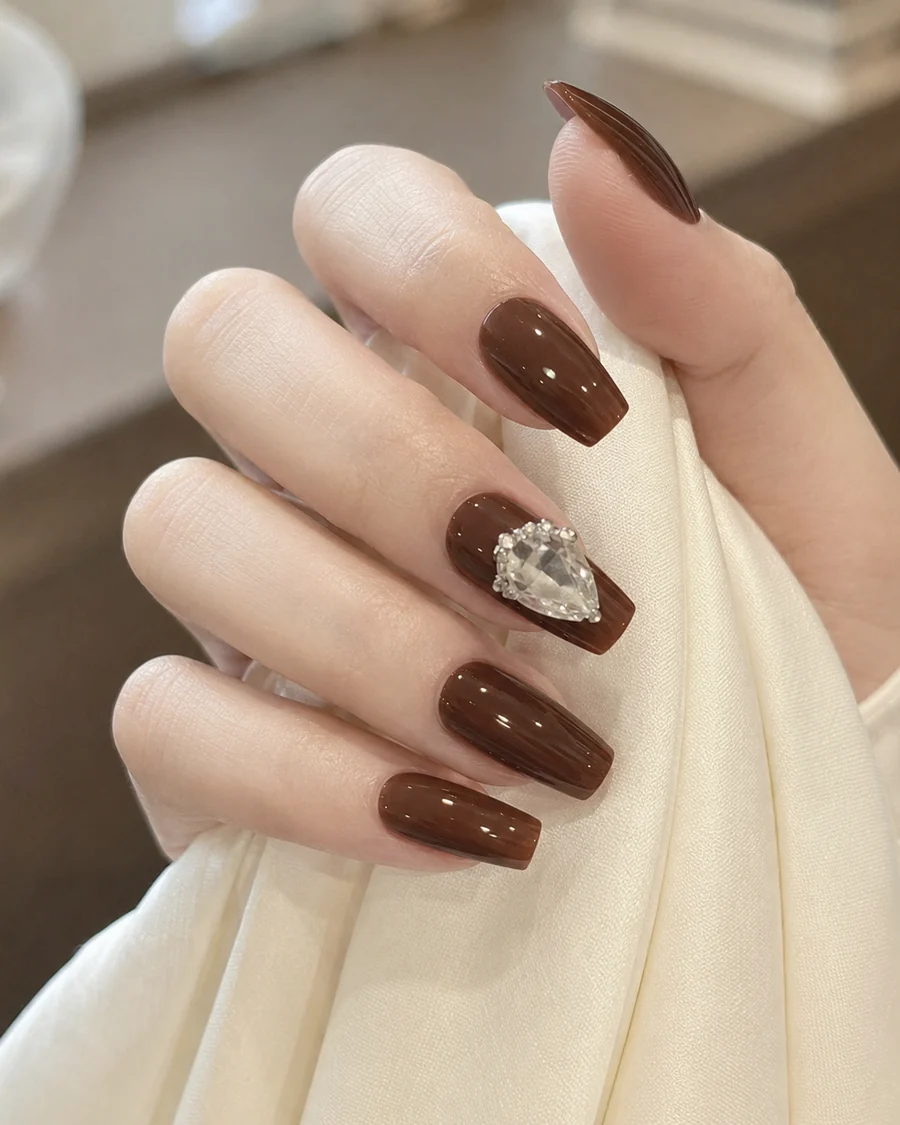 Manicura chocolate con forma cuadrada y detalle de joya